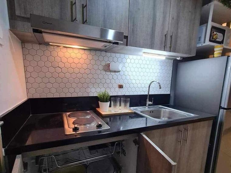 Completed compact kitchen with hexagonal tile splashback, range hood, under-cabinet lighting and pull-out storage