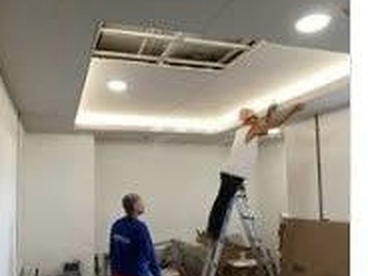 Ceiling cassette air-conditioning unit being installed by crew on a ladder