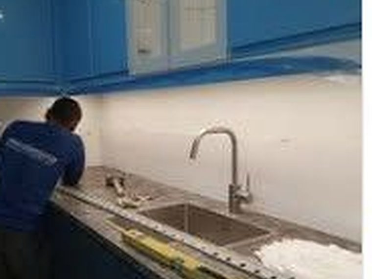 Kitchen counter, sink and mixer tap being set and levelled against a tiled splashback